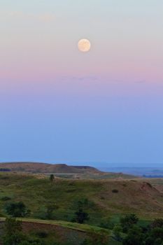 The full moon rises over the prairie hills.