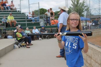 Ten-year-old Chloe Holzwarth displays the Sam Bat for the crowd while auctioneer Lanning Edwards takes bids between games of the state amateur baseball tournament in Mitchell Saturday. Photo by Craig Wenzel/Wessington Springs True Dakotan